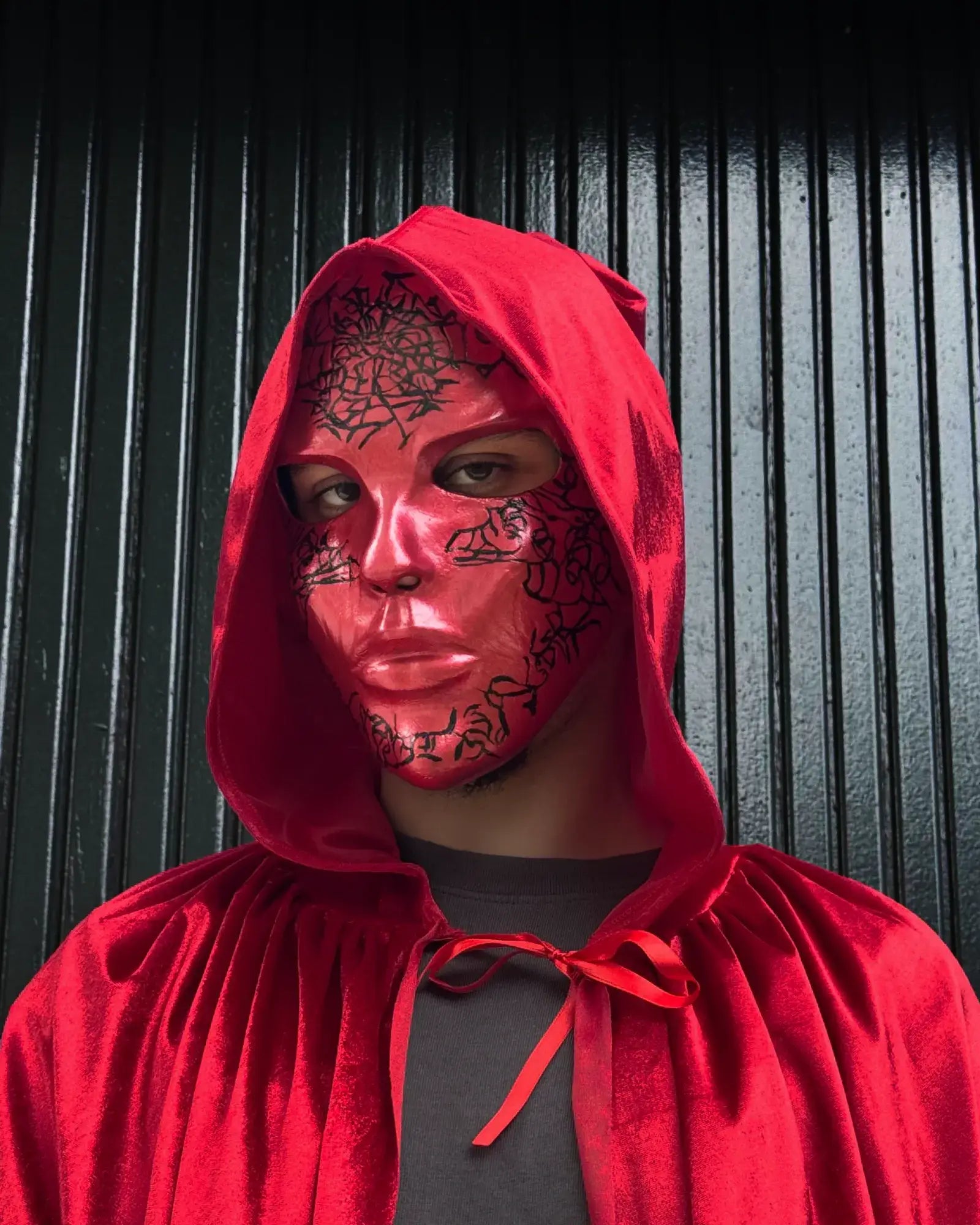 Person wearing Abstract Crackle look black pattern; Handmade Red Masquerade Mask with red cape, handcrafted Venetian cosplay accessory.