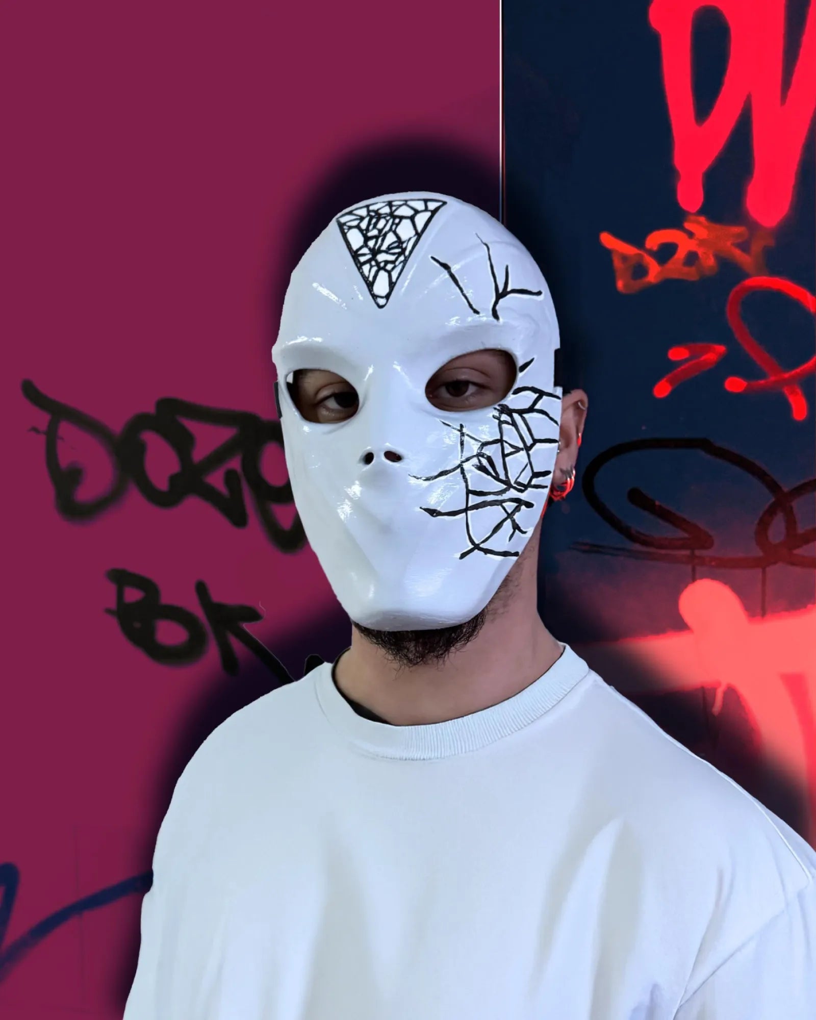 Person wearing Conspirator Venetian Black Crackle Pattern; Graffiti Style White Mask against graffiti background, handcrafted cosplay accessory.