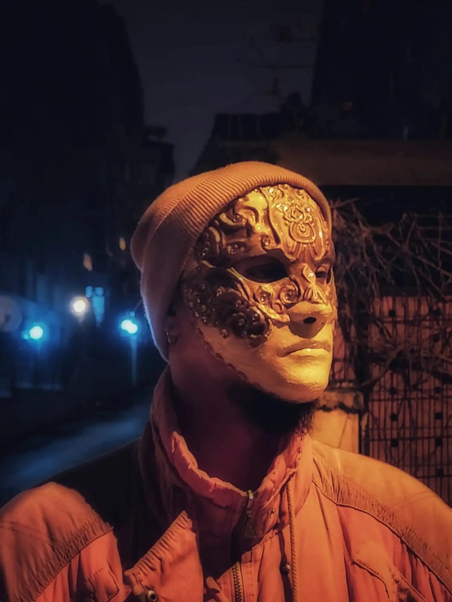 Gold ornate mask with intricate patterns and a brown knit beanie.