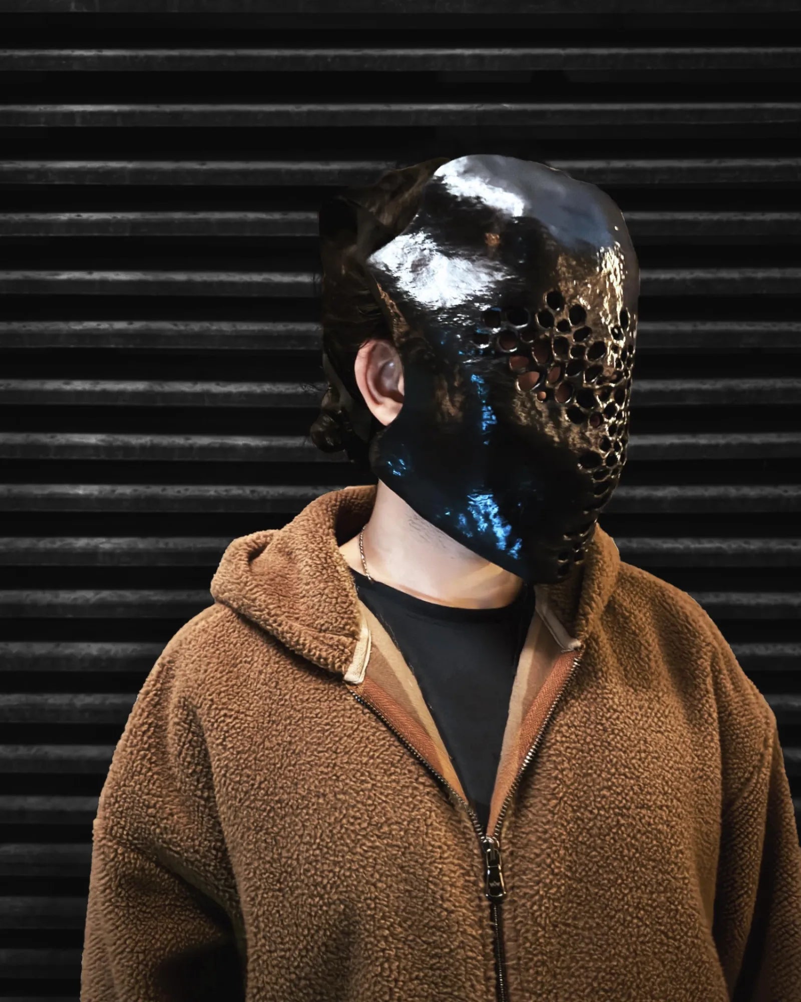 Symbiotic Trypophobia Venom; Alien Perforated Black Mask handcrafted venetian cosplay fantasy mask worn by person against ridged background.