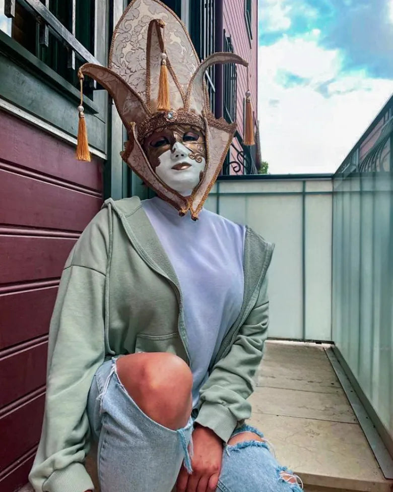 Person wearing The Popess - Luxurious White and Gold Chic Art Venetian Mask for Masquerade, in casual outfit, on a terrace.