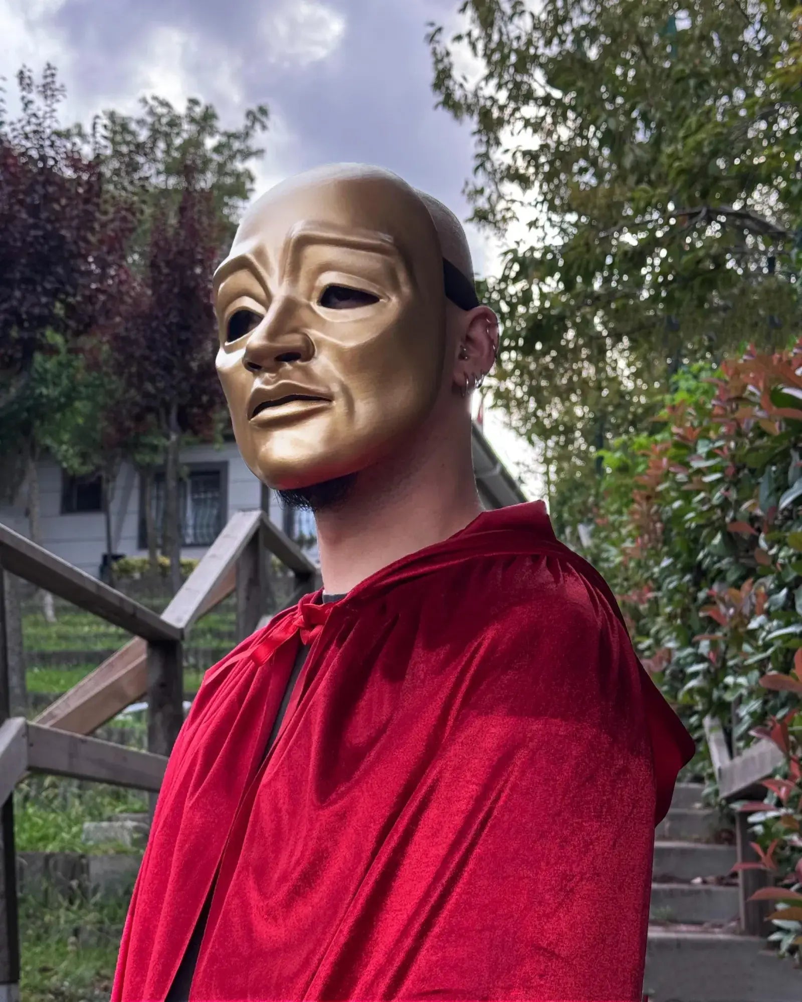 Eyes Wide Shut Red Velvet Hooded Cloak; Inspired Cape Cloak worn with a golden Venetian mask in a lush outdoor setting.