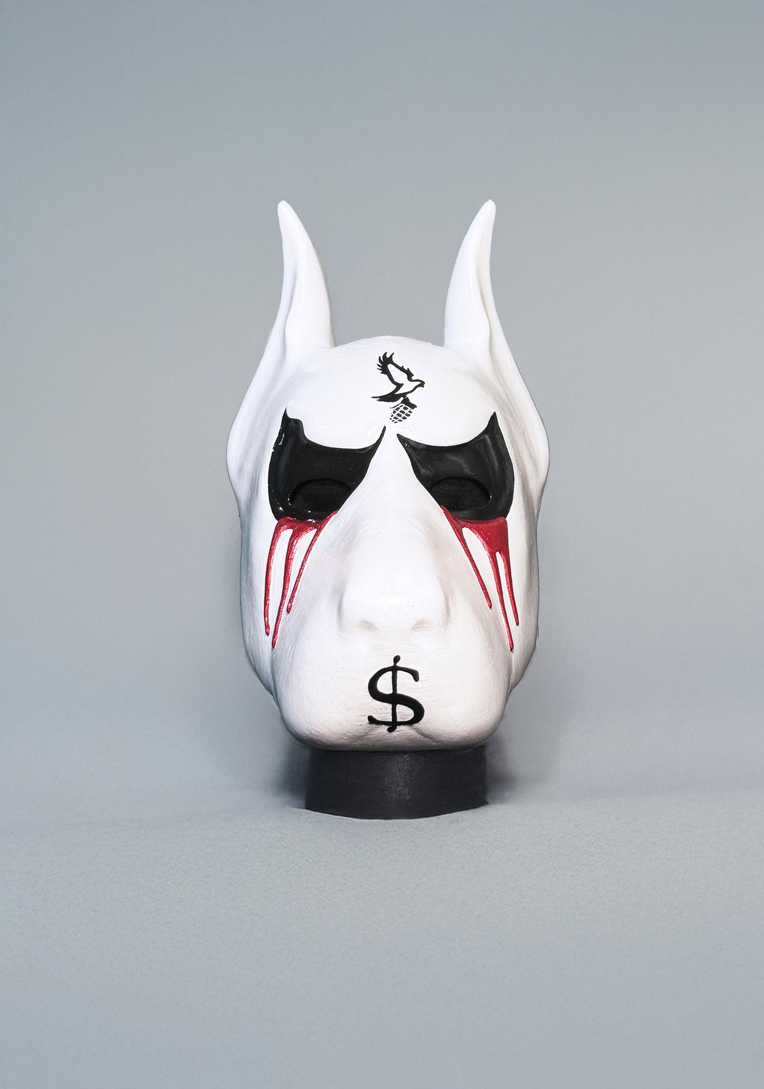 May include: A white dog mask with black eyes, a black bird design on the forehead, and a red dollar sign on the snout.